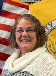 woman wearing glasses and a white/gray colorblock sweater in front of an American flag