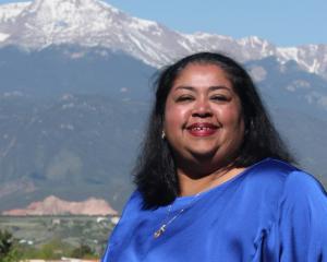 woman with hair past her shoulder in a blue shirt in front of a mountain landscape